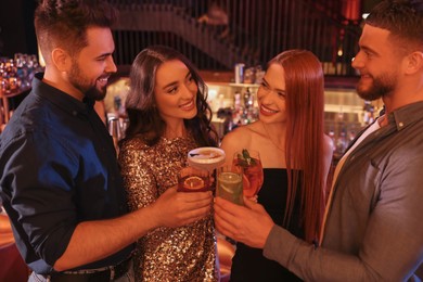 Photo of Happy friends clinking glasses with fresh cocktails in bar