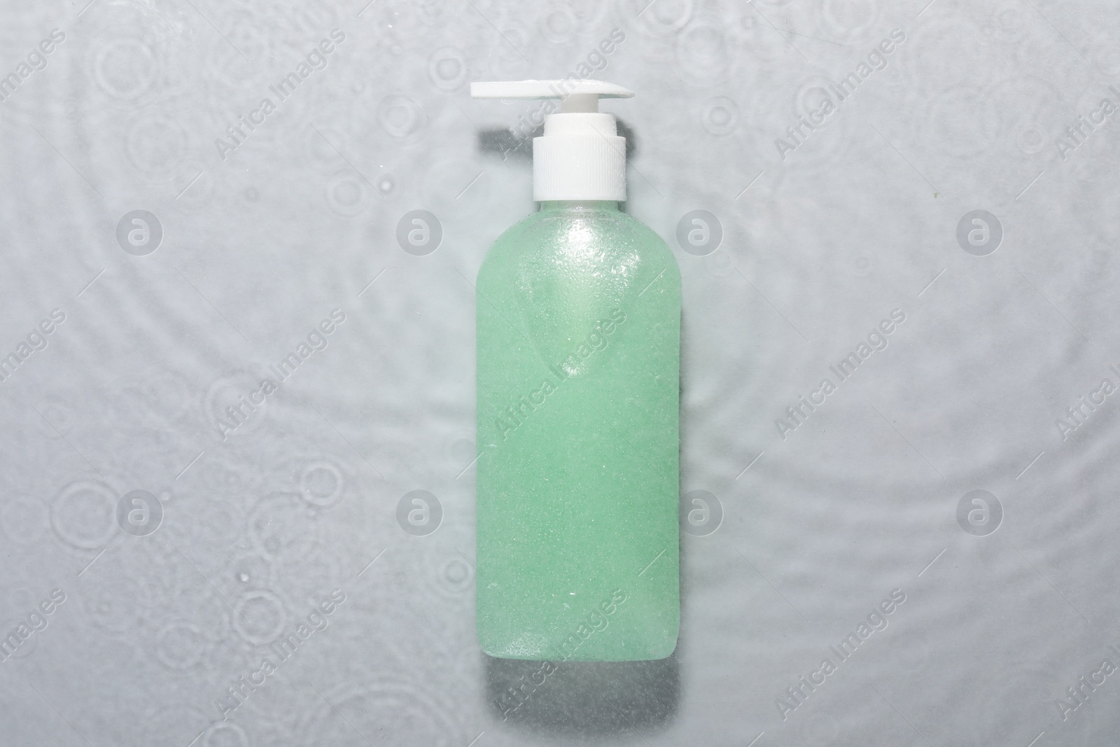 Photo of Bottle of facial cleanser in water against light grey background, top view