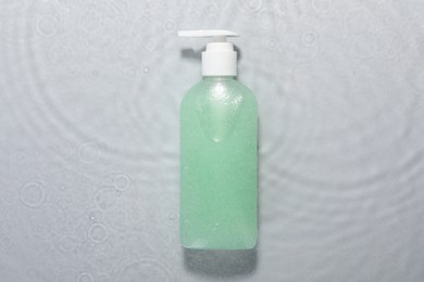 Bottle of facial cleanser in water against light grey background, top view