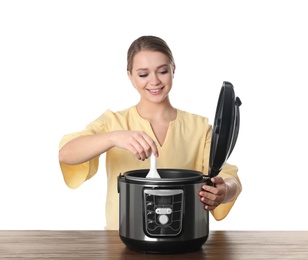 Young woman preparing food with modern multi cooker at table against white background