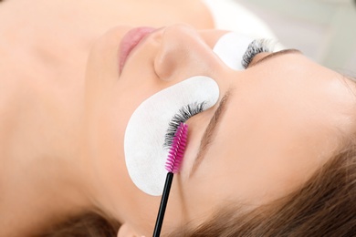 Photo of Young woman undergoing eyelash extensions procedure, closeup