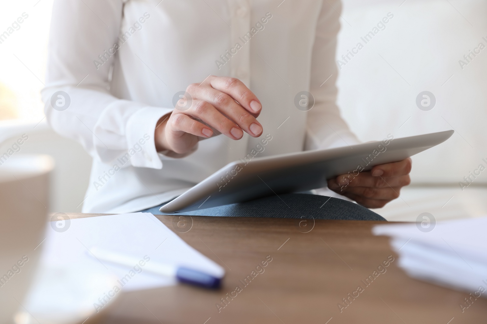 Photo of Businesswoman working with modern tablet at wooden table in office, closeup