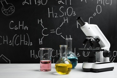 Photo of Laboratory glassware and microscope on table against blackboard with chemical formulas