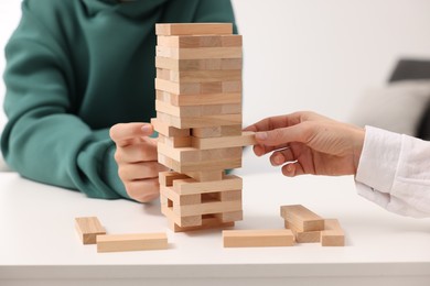 Photo of People playing Jenga tower at white table indoors, closeup