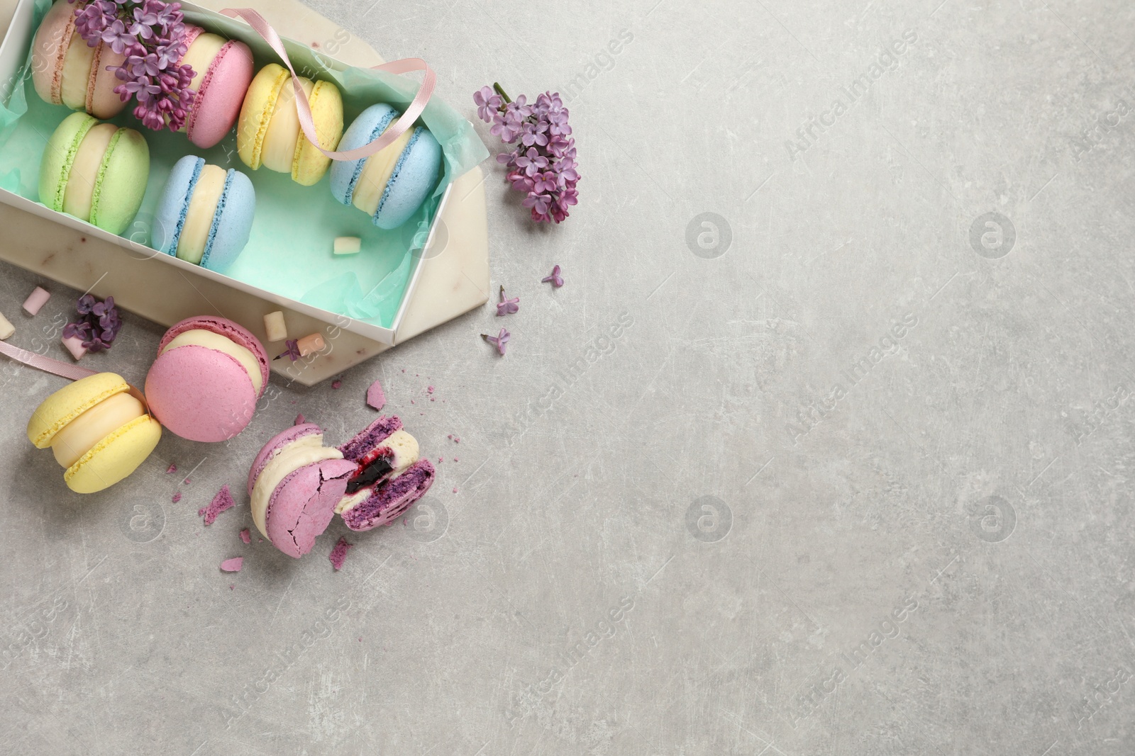 Photo of Delicious colorful macarons, marshmallows and lilac flowers on grey table, flat lay. Space for text