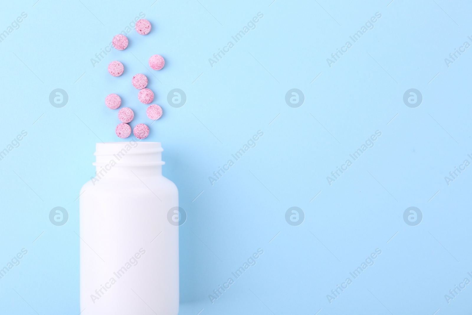 Photo of Jar with vitamin pills on light blue background, top view. Space for text