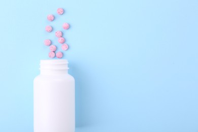 Photo of Jar with vitamin pills on light blue background, top view. Space for text