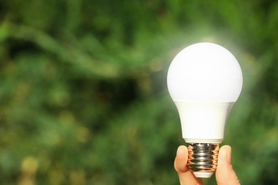 Image of Woman holding glowing light bulb outdoors, closeup. Space for text