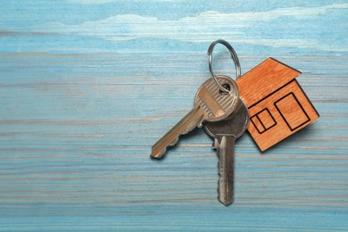 Photo of Keys with trinket in shape of house on light blue wooden table, top view and space for text. Housewarming party