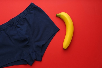 Men's underwear and banana on red background, flat lay. Potency problem concept