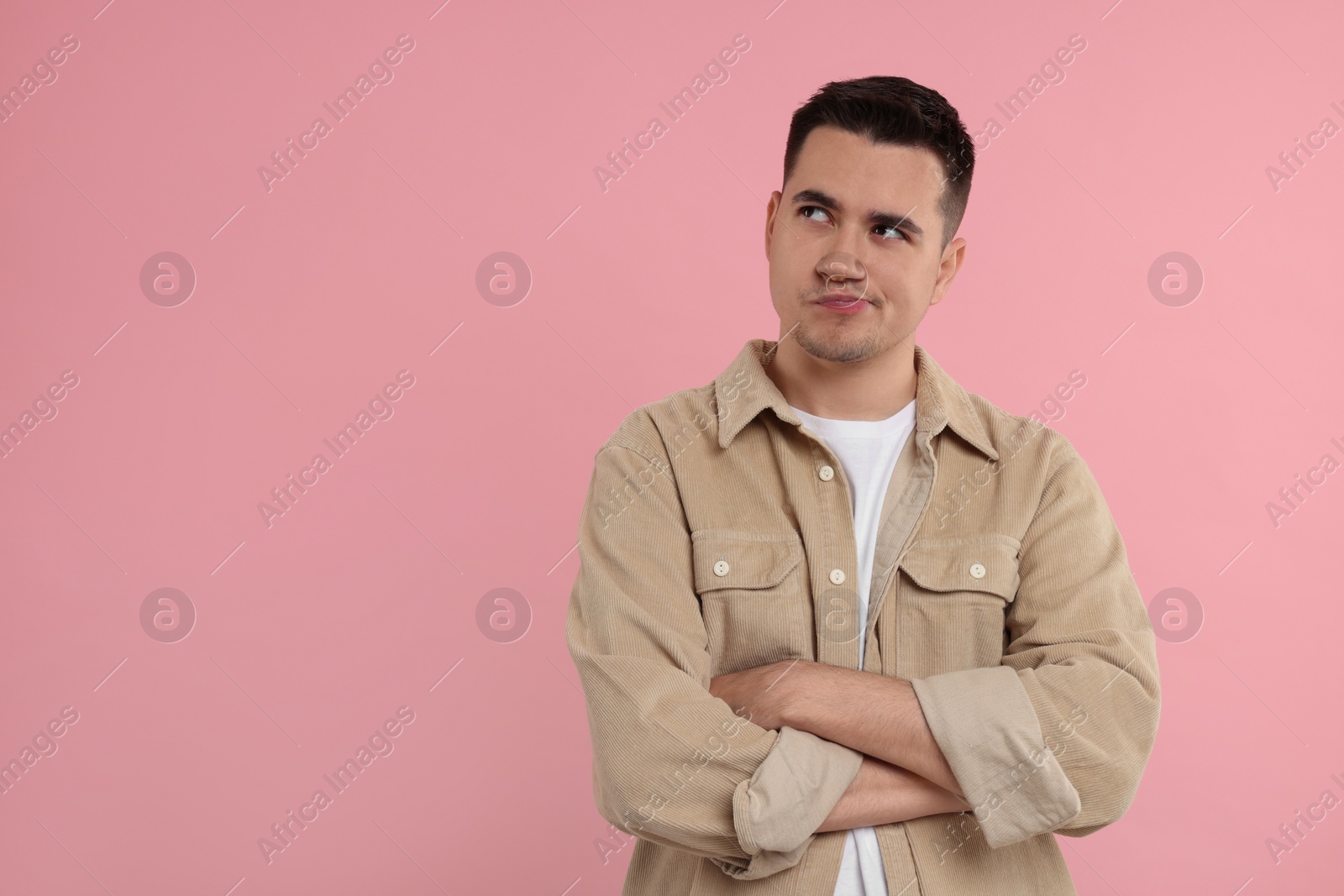 Photo of Resentful man with crossed arms on pink background, space for text