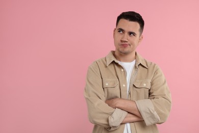 Resentful man with crossed arms on pink background, space for text