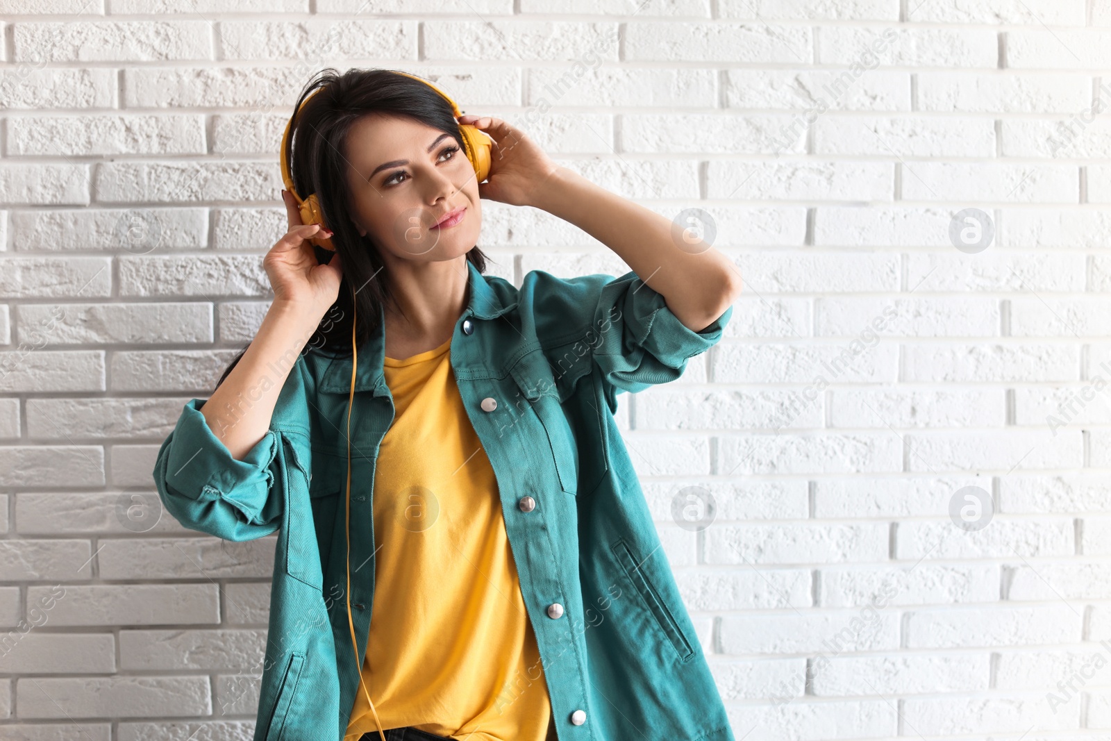 Photo of Portrait of beautiful woman listening to music with headphones near brick wall. Space for text