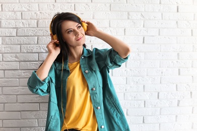 Portrait of beautiful woman listening to music with headphones near brick wall. Space for text