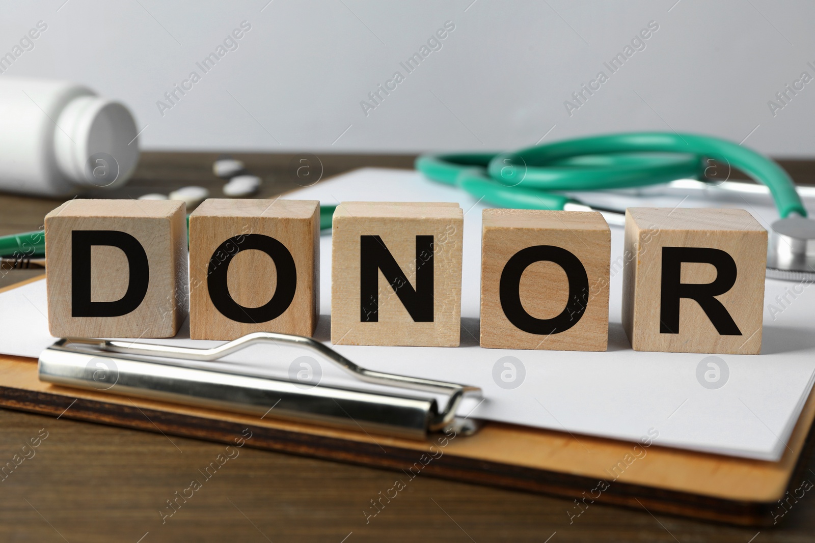 Photo of Word Donor made of cubes, clipboard and stethoscope on wooden table, closeup