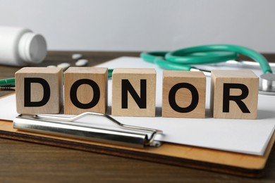 Photo of Word Donor made of cubes, clipboard and stethoscope on wooden table, closeup