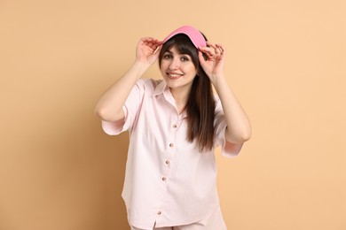 Happy woman in pyjama and sleep mask on beige background