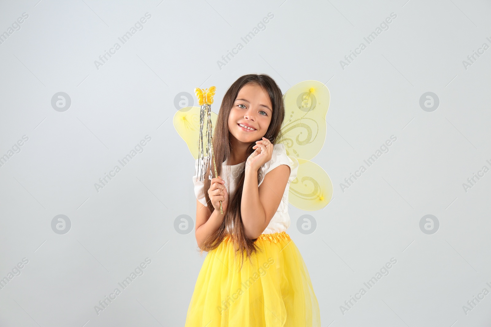 Photo of Cute little girl in fairy costume with yellow wings and magic wand on light background