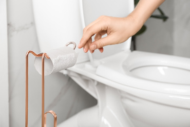 Photo of Woman reaching for empty toilet paper roll in bathroom, closeup