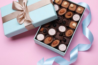 Photo of Open box of delicious chocolate candies on pink background, closeup