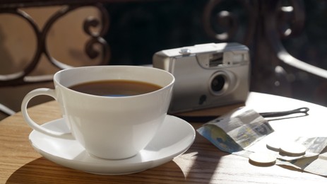 Cup of aromatic coffee, banknotes and camera on wooden table outdoors