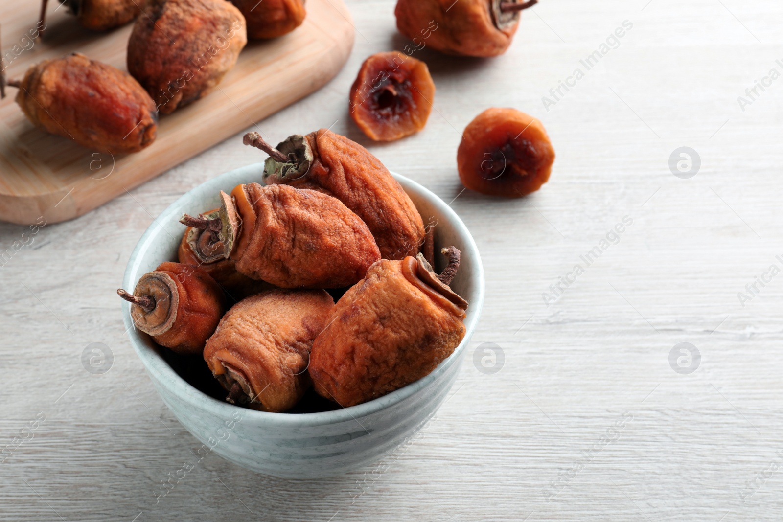 Photo of Bowl with tasty dried persimmon fruits on wooden table, space for text