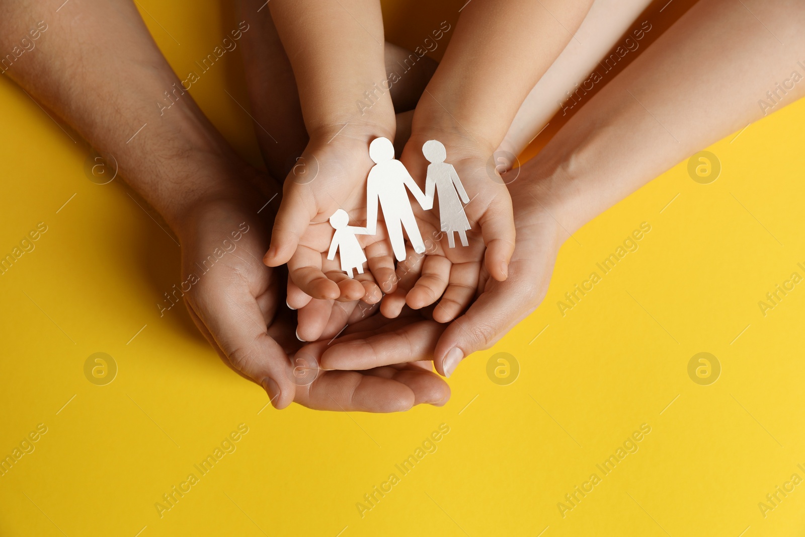 Photo of Parents and child holding paper cutout of family on yellow background, top view
