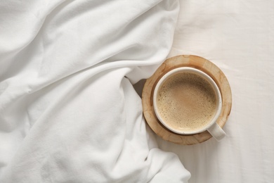 Photo of Cup of aromatic coffee on bed with soft blanket, top view. Space for text