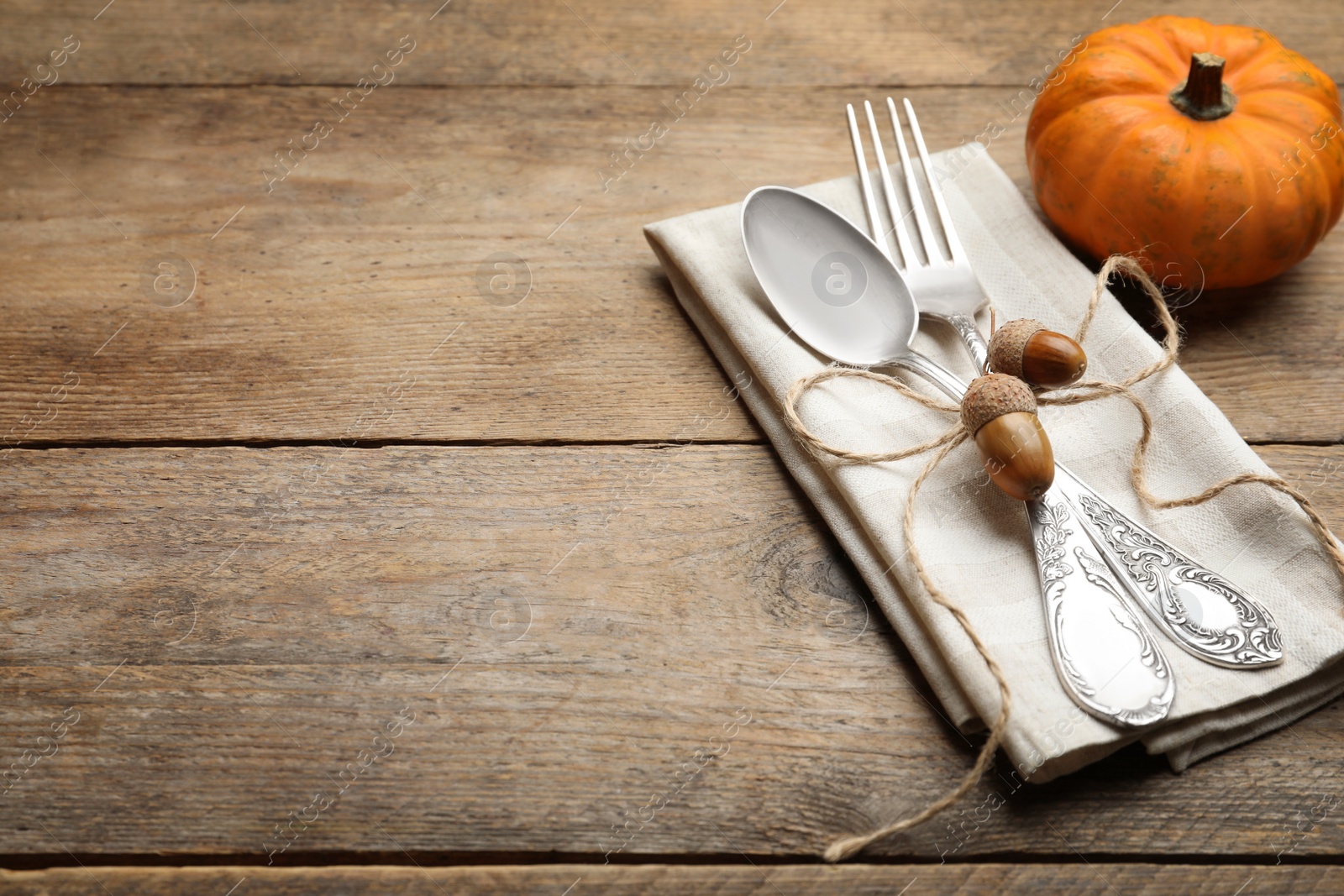 Photo of Autumn table setting, space for text. Cutlery with napkin, acorns and pumpkin on wooden background