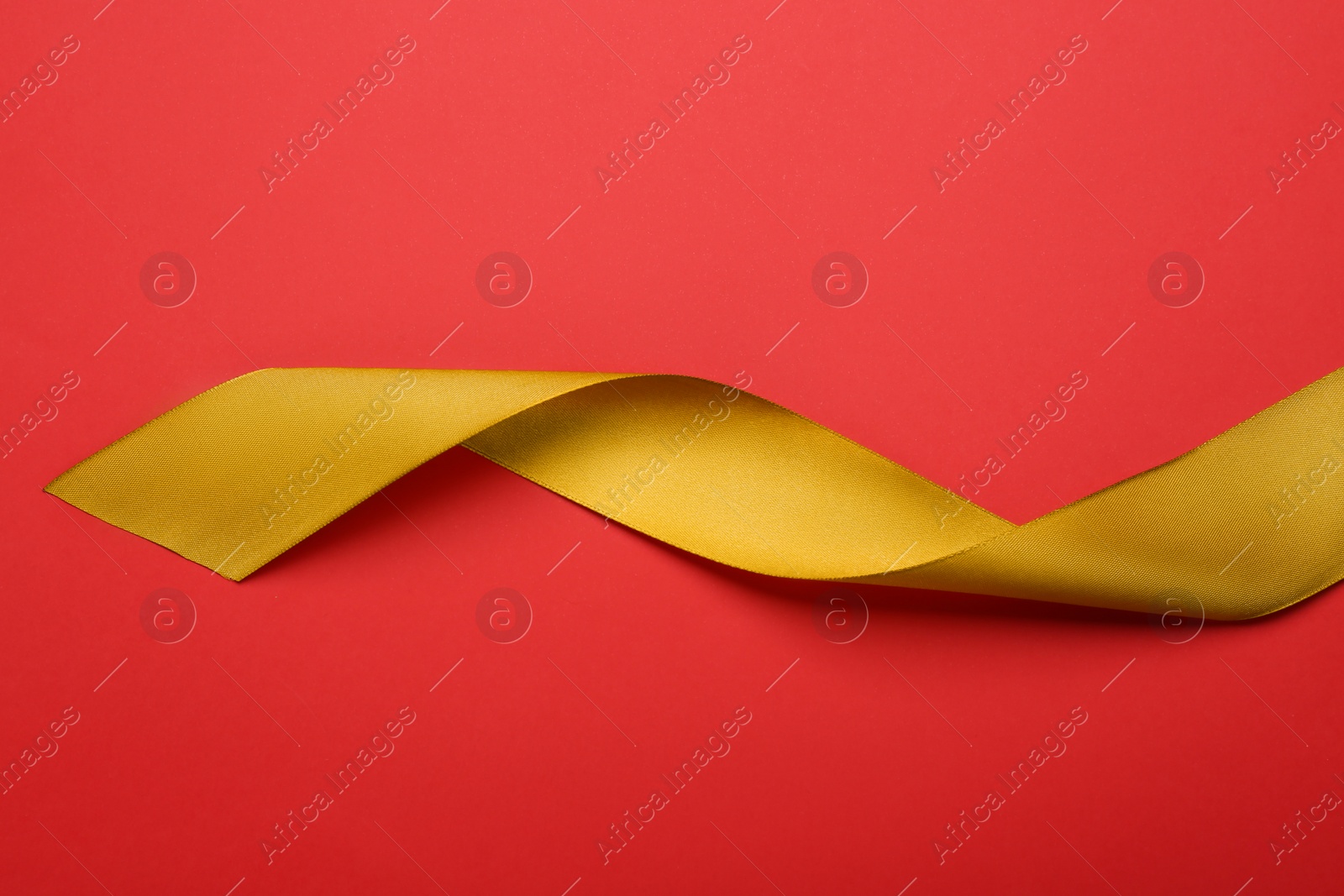 Photo of Beautiful golden ribbon on red background, top view