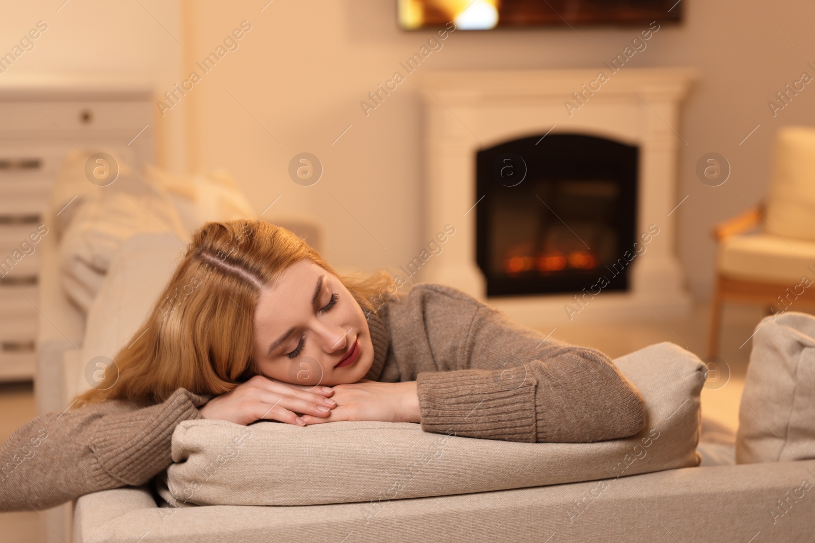 Photo of Beautiful young woman resting near fireplace at home