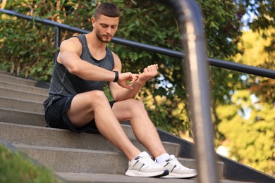 Photo of Attractive serious man checking pulse after training on stairs in park