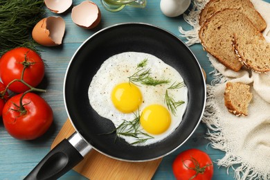 Frying pan with tasty cooked eggs, dill and other products on light blue wooden table, flat lay