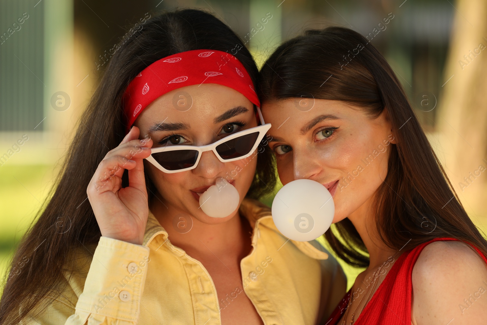 Photo of Beautiful young women blowing bubble gums outdoors