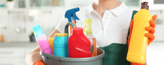 Image of Closeup view of woman with detergents and bottle in kitchen, banner design. Cleaning service
