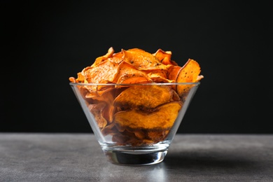 Photo of Bowl with sweet potato chips on table against black background