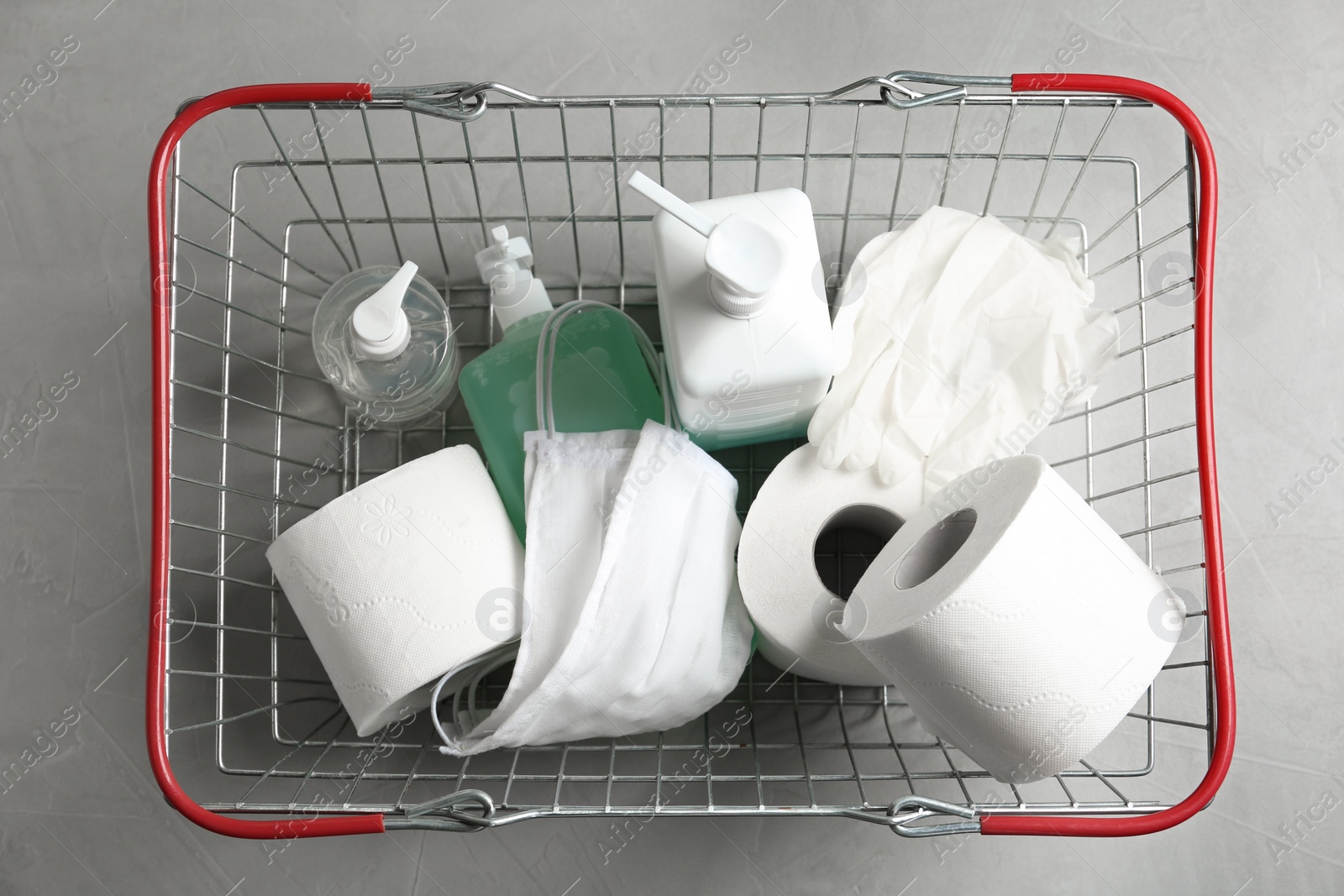 Photo of Shopping basket with antiseptics, toilet paper, gloves and masks on light grey stone table, top view. Panic caused by virus