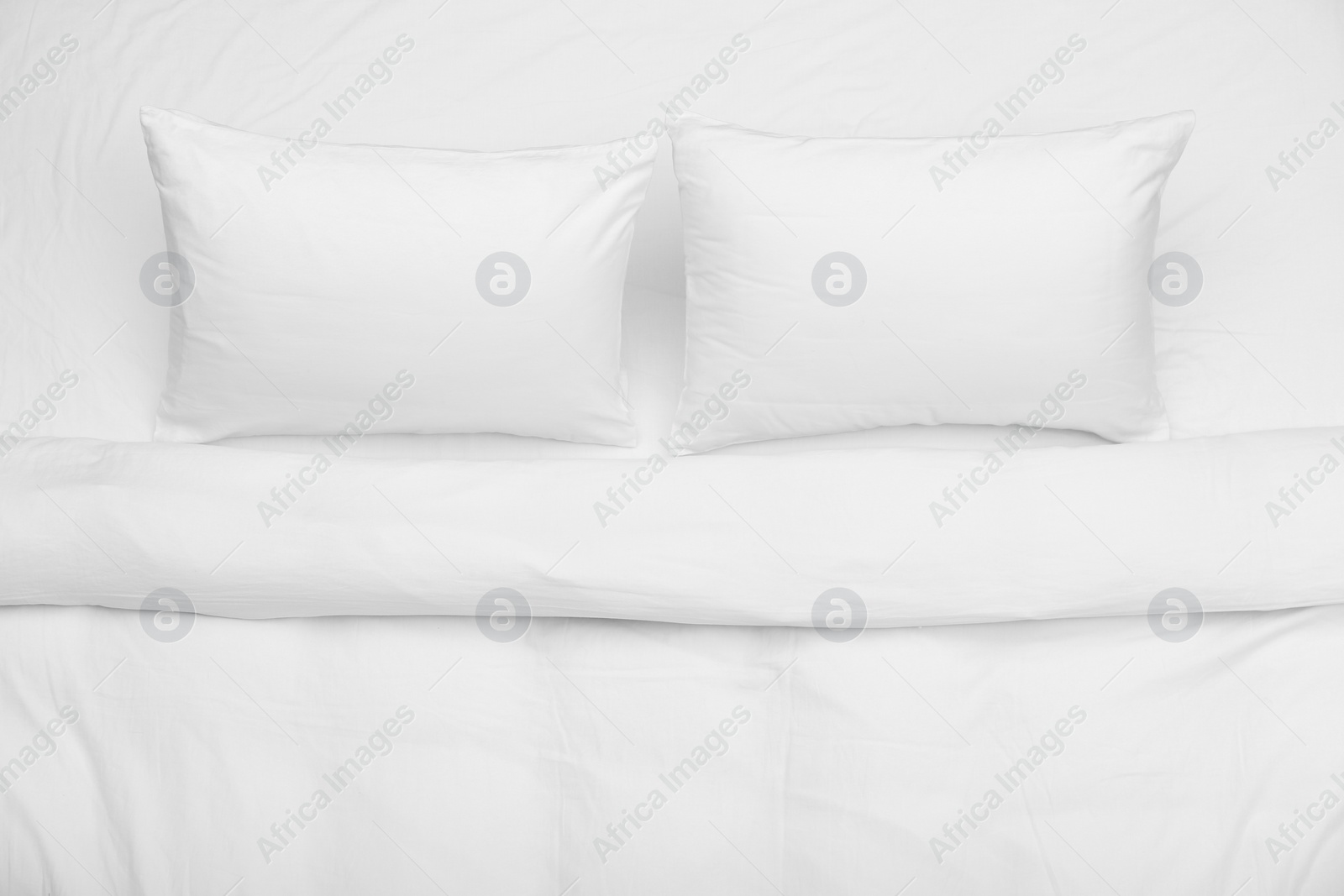 Photo of Soft white pillows and blanket on bed, top view