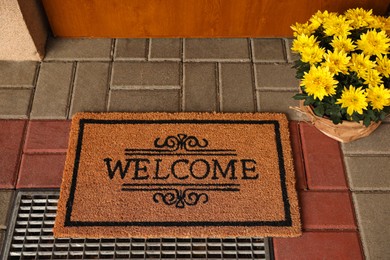 Photo of Door mat with word Welcome and beautiful flowers near entrance