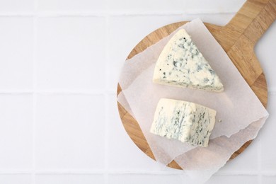 Photo of Wooden cutting board with blue cheese on white tiled table, top view. Space for text