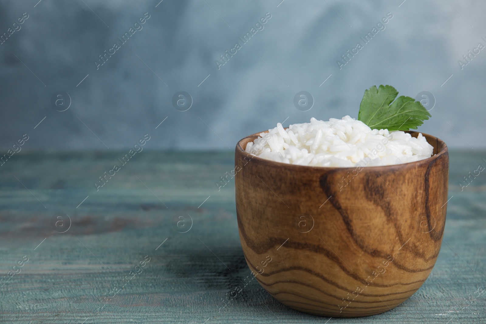 Photo of Bowl with tasty cooked rice on light blue wooden table. Space for text
