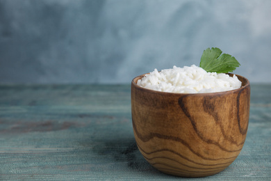 Bowl with tasty cooked rice on light blue wooden table. Space for text