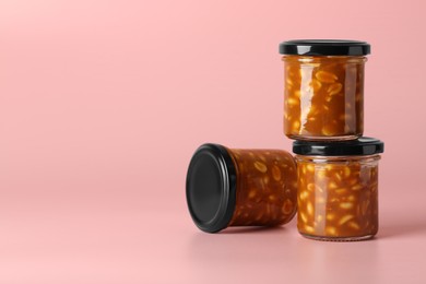 Tasty salted caramel with peanuts in jars on pink background, space for text