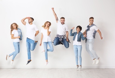 Photo of Group of young people in jeans jumping near light wall