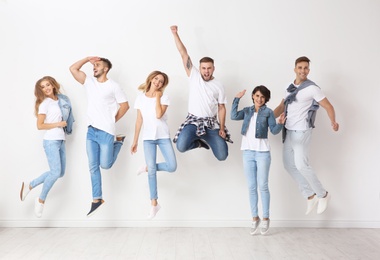 Group of young people in jeans jumping near light wall