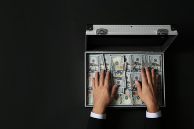 Businessman with suitcase full of money on dark background, top view