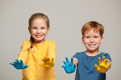 Photo of Little girl and boy with hands painted in Ukrainian flag colors on light grey background. Love Ukraine concept