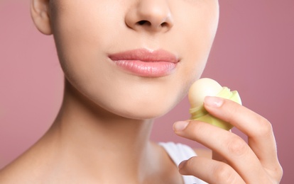 Young woman applying balm on her lips against color background, closeup