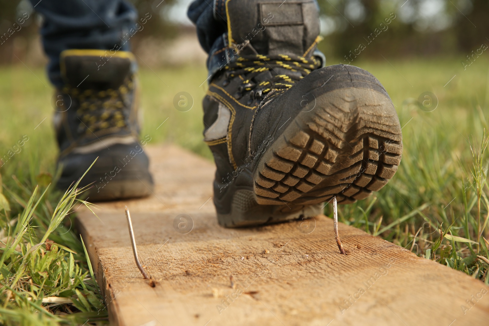 Photo of Careless worker stepping on nail in wooden plank outdoors, closeup