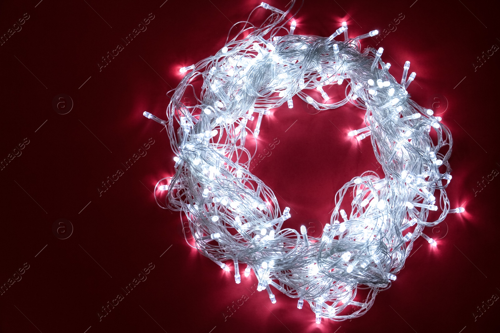 Photo of Frame made of glowing Christmas lights on burgundy background, top view. Space for text